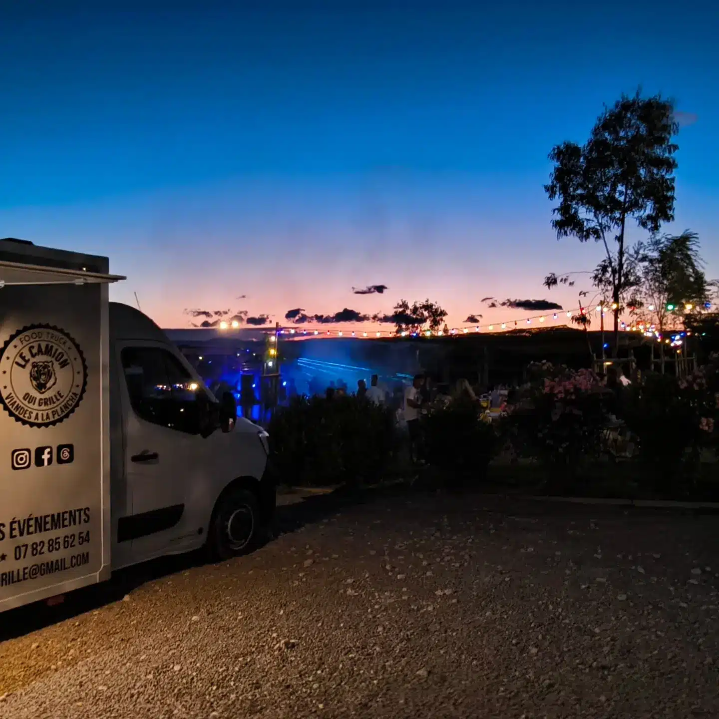 Food truck "LE CAMION QUI GRILLE" lors d'un événement extérieur au crépuscule avec guirlandes lumineuses.